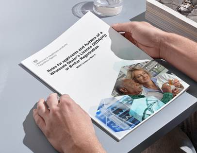 Someone holding a document entitled 'Notes for applicants and holders of a Wholesale Distribution Licence (WDA) or Broker Registration.' on a grey table. Life Science Consulting